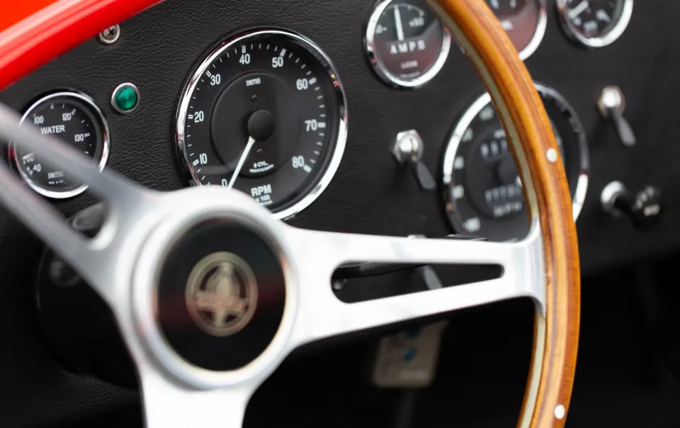 Close-up of a classic roadster cockpit: a wood-rimmed steering wheel with chrome spokes in front of round analog gauges